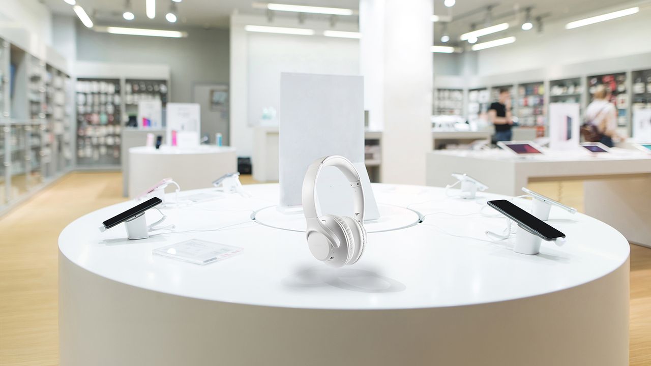 Tecnología y gadgets en vitrina para compra o revisión Audífonos blancos en exhibición junto a celulares en una tienda de tecnología moderna
